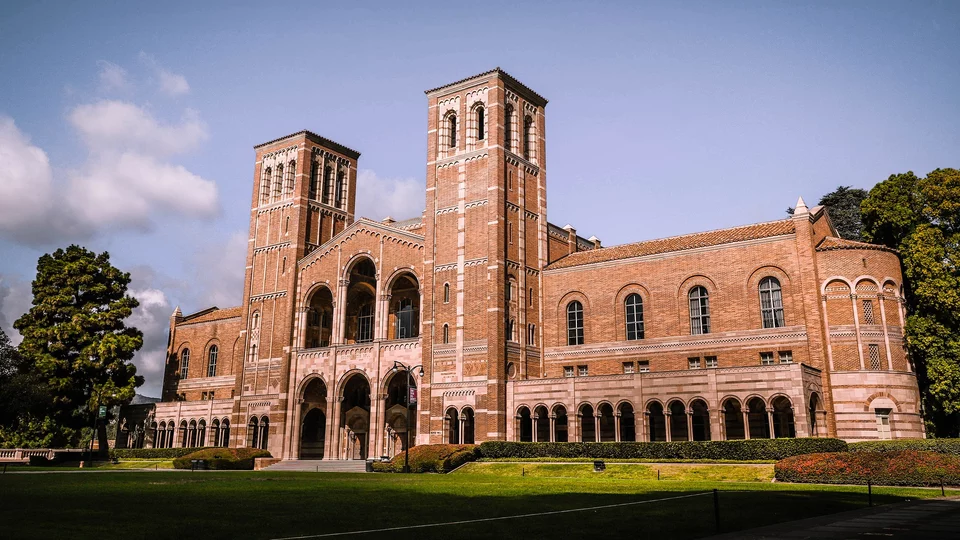 University building with two towers in front of grassy campus.